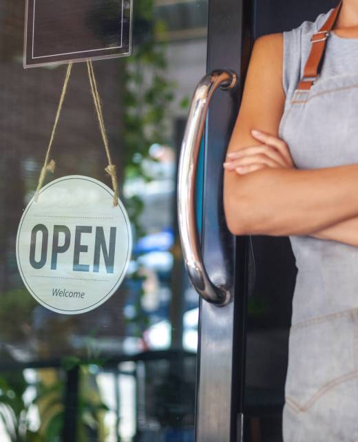 The woman is a waitress in an apron, the owner of the cafe stands at the door with a sign Open waiting for customers. Small business concept, cafes and restaurants